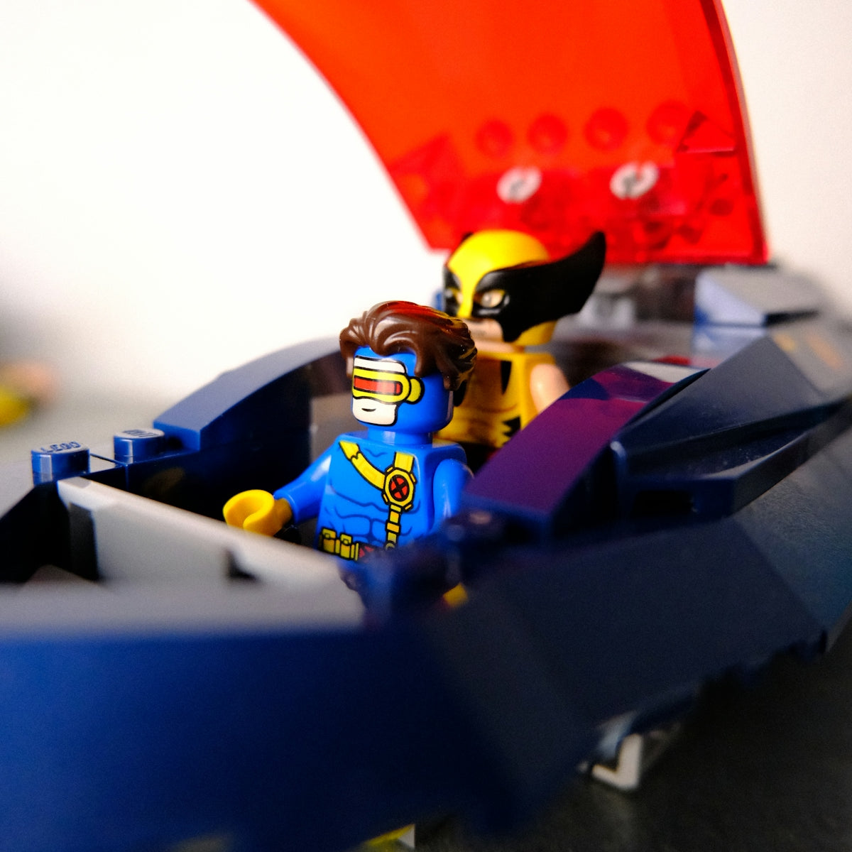 Cyclops and wolverine lego minifigures in a blue vehicle.